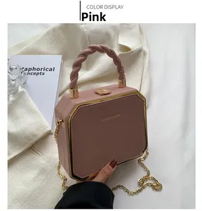 Close-up of pink hexagonal handbag with spiral handle and gold chain on white fabric