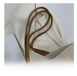 Close-up of brown leather handles on a minimalist beige tote bag with neat stitching