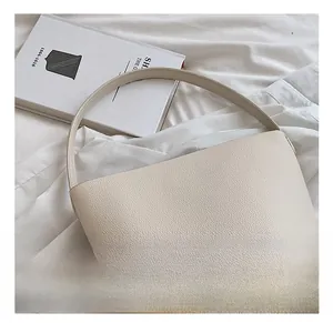 Close-up of beige lychee texture leather handbag with minimalist handles on a white book