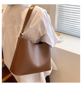 Brown leather tote bag featuring wide shoulder straps and side metal rivets on lifestyle setting