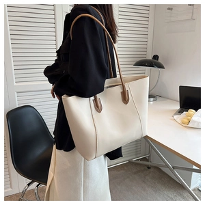 Detail of a large beige tote bag with brown straps in a minimalist office setting