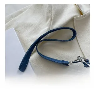 Dettaglio tracolla in denim blu con cuciture bianche e chiusura a moschettone argentata