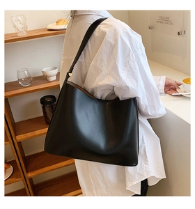 Side view of a large black leather tote bag worn by a model in a modern cafe setting