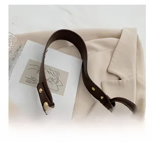Détail de la poignée du sac en cuir marron avec rivet doré sur fond de blazer beige