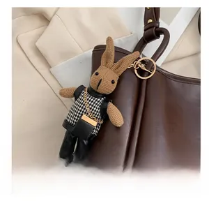 Détail d'un porte-clé lapin tricoté avec gilet pied-de-poule sur un sac en cuir brun
