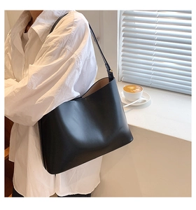 Close-up of a black matte leather tote bag worn by a model in a cozy cafe setting