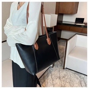 Detail of black tote bag with brown leather straps and contrast white stitching trim
