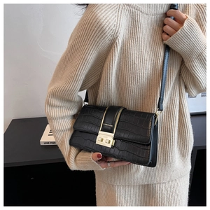 Detail of black crocodile texture bag with gold clasp shown on a model outfit