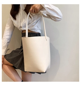 Detailed view of cream white bucket bag in lychee pattern faux leather worn by a model