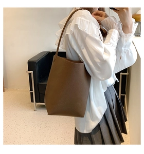 Detail view of a large brown textured leather tote bag worn by a model in a minimal setting