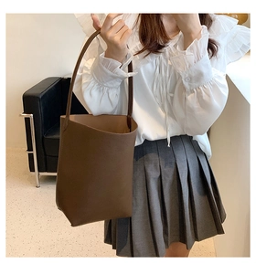 Brown leather bucket bag styled with a white ruffled shirt and pleated skirt
