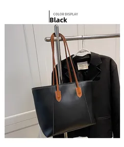 Detail view of large black leather tote bag with brown straps and white decorative stitching