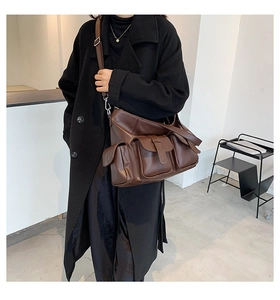 Detail of a brown large capacity tote bag with triple utility pockets and buckled straps