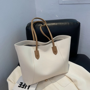 Minimalist large white tote bag with brown long handles on a modern black leather chair
