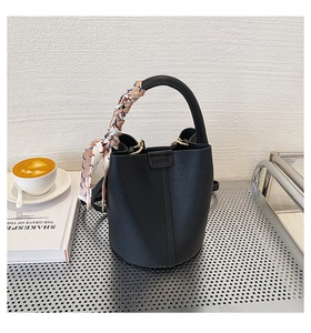 Close-up of black lychee leather bucket bag with silk scarf on handle and coffee