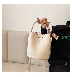 Close-up of beige lychee grain leather bucket bag with pink silk scarf on handle