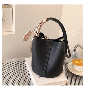 Detailed close-up of black lychee leather bucket bag with elegant beige silk scarf handle