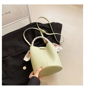 Detail of light green litchi grain leather bucket bag with silk scarf handle on black suit