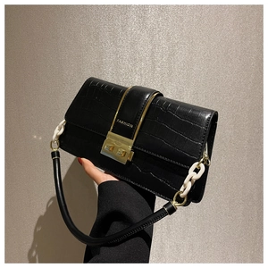 Detail of black crocodile texture handbag with gold buckle and resin chain strap
