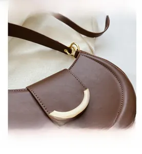 Detailansicht einer braunen matten Satteltasche aus Leder mit goldener Schließe und Nähten