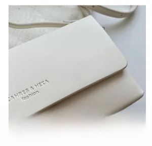 Detailed macro view of cream leather texture and embossed logo on the small crossbody bag