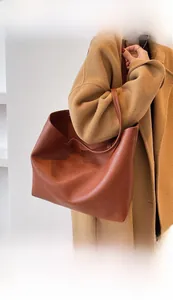 Brown leather tote bag worn over the shoulder showing minimalist texture and large capacity