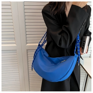 Detail of blue crescent crossbody bag with thick multi-colored rope strap on shoulder