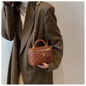 Close-up of quilted brown leather box bag with gold floral detail and chain strap