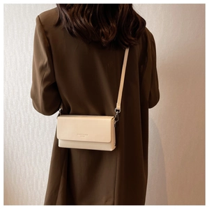 Detail view of cream white minimalist crossbody bag worn with a wool coat
