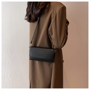 Minimalist black matte leather crossbody bag with silver buckle worn with a beige trench coat