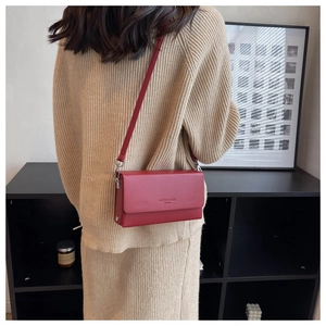 Detail of burgundy leather shoulder bag with gold lettering shown on a female model