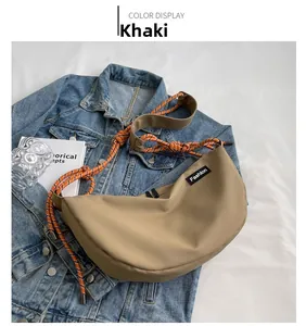 Detail of khaki crescent crossbody bag with orange woven rope strap and Fashion label