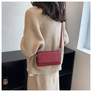 Detail of red leather crossbody bag with flap and embossed logo worn with a beige sweater