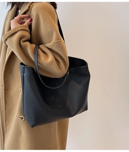 Detailed texture of black pebbled leather tote bag worn with a camel coat for work