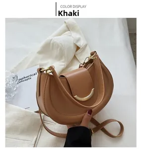 Detail of khaki crescent shoulder bag with golden half-moon buckle against white blazer