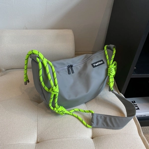 Grey oxford fabric crossbody bag with neon green rope strap on a beige sofa