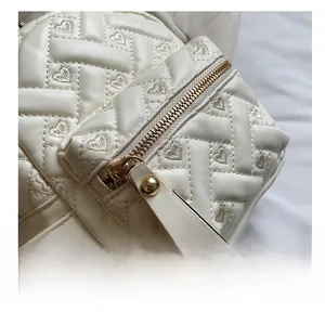 Macro detail of smooth golden zipper and heart embroidery on white quilted backpack