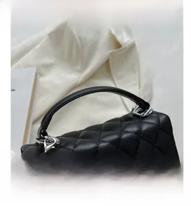 Detail of black quilted shoulder bag with a silver lion pendant and leather texture