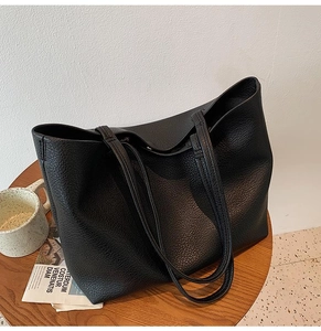 Top-down view of black pebbled leather tote bag with long shoulder straps on a wooden table