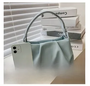 Detail view of light blue pleated cloud bag compared to a phone for size reference