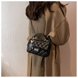 Detail of black quilted shoulder bag with silver robot charm and twist-lock closure