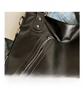 Detailed close-up of a black leather tote bag showing side zipper pocket and stud rivets
