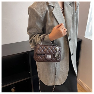 Detail of a brown quilted crossbody bag with a chain strap and a silver robot charm