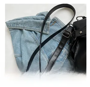 Close-up of adjustable black leather strap with silver buckle on a textured tote bag