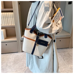 Detailed side view of off-white canvas bucket bag with leather trim worn by model