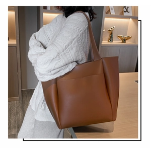 Brown leather tote bag detail with wide shoulder strap worn over a white sweater