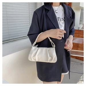 Close-up of cream ruched underarm bag featuring vertical pleats and a unique knot handle