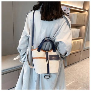 Dettaglio borsa a secchiello in tela con finiture in pelle blu indossata da una modella