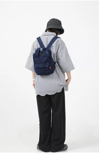 Detail of deep blue denim backpack with zipper pockets on a model for casual outdoor wear