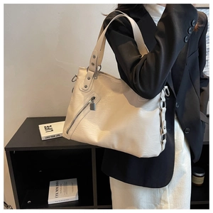 Detail of off-white tote bag showing textured leather, metal studs, and decorative zipper